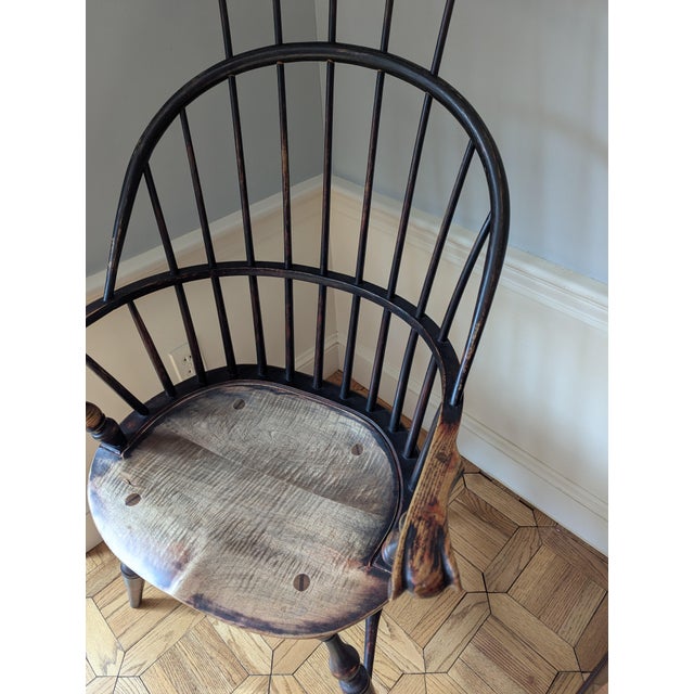 This appears to be a traditional comb-back Windsor armchair featuring a historic distressed black-painted finish and a...