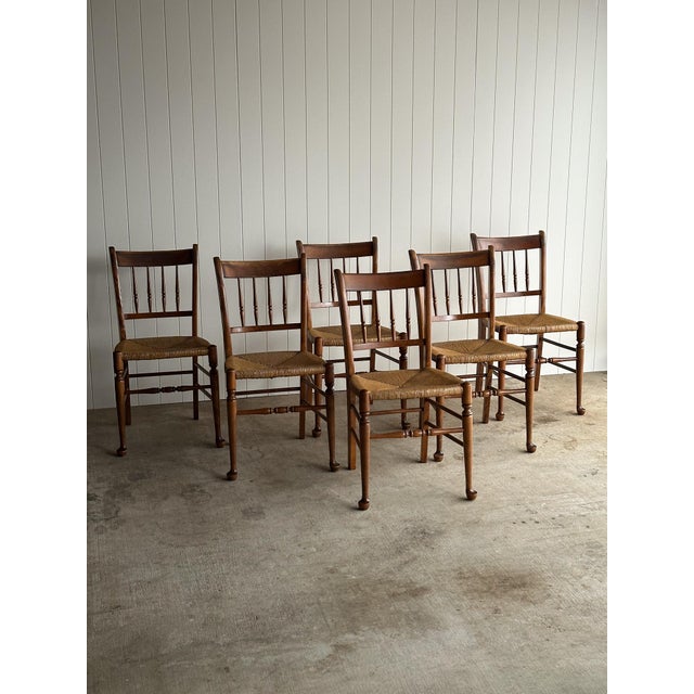 Set of six vintage dining chairs crafted with solid maple frames, spindle backs, and hand-woven rush seats. Warm, time-...