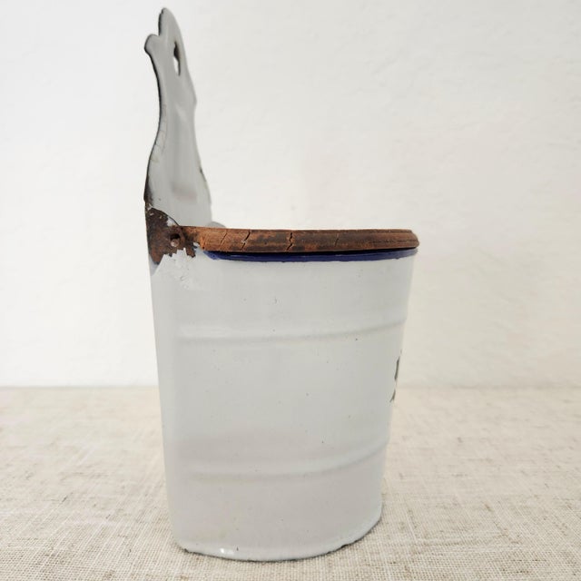 A vintage enamelware salt box cellar from Germany with a hinged wood lid; can be hung on a wall. The vintage patina is...