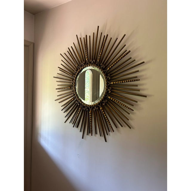 Stunning, large sunburst mirror in gilt wrought iron. Round beveled mirror measures 13” in diameter. Features a 1”frame...