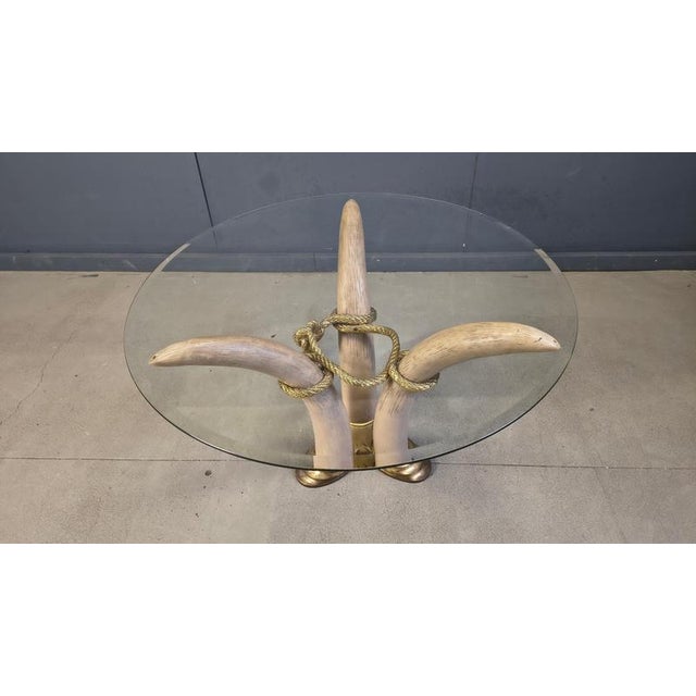 Elegant center table featuring faux elephant tusks made from resin mounted on a brass base with a round beveled glass top....