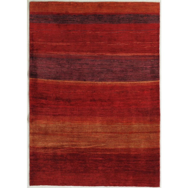 Hand-knotted Persian Lori Gabbeh rug featuring a field composed of horizontal bands in tonal red and rust hues, with...