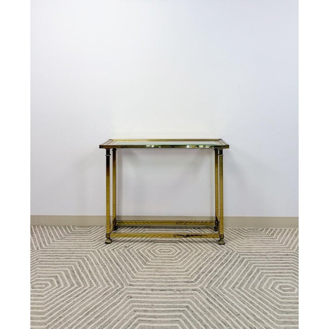 Add timeless elegance to your space with this vintage mid-century modern brass console table featuring a sleek glass top....