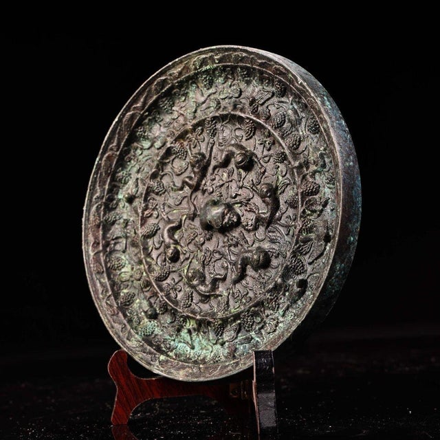 This is a cast bronze mirror featuring a highly detailed relief decoration on one side and a plain, patinated surface on...