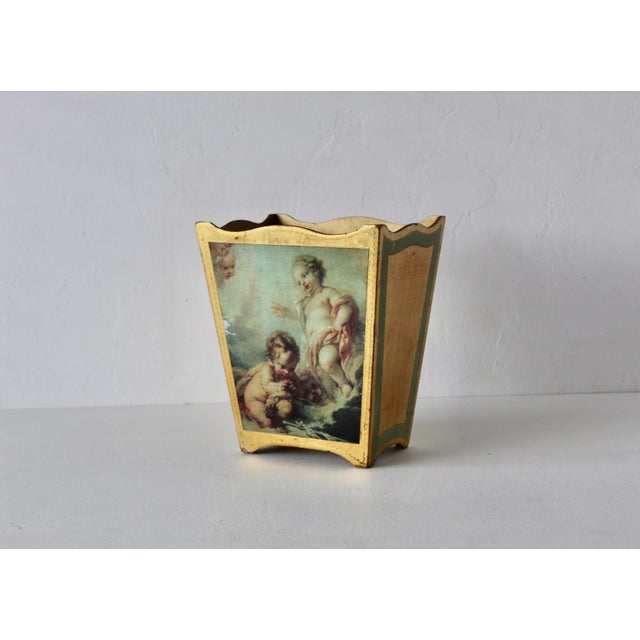 A Florentine wastebasket features a gold-gilt finish with a decoupage scene of cherubs. In good vintage condition with...