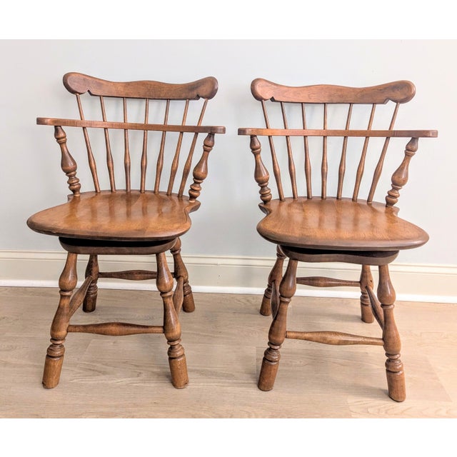 This is a pair of solid maple swivel dining chairs are in the Colonial Windsor style, with a comb back and saddle seat....