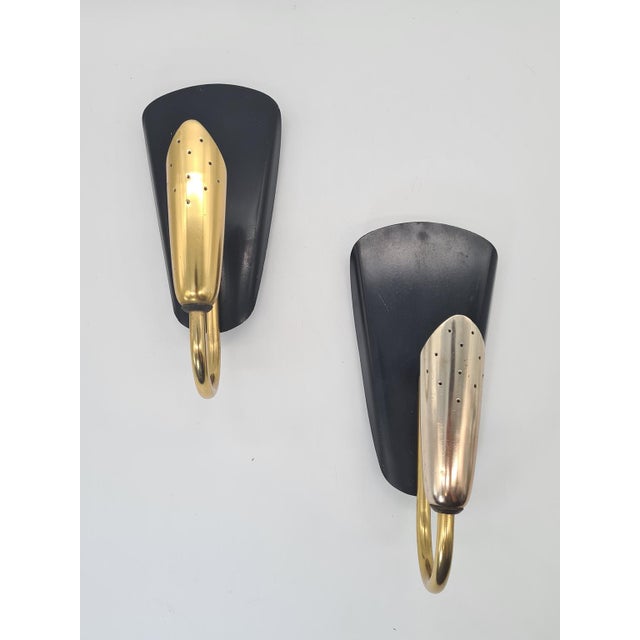 A striking pair of modernist-style wall sconces from the 1970s, crafted from black lacquered metal and brass accents. The...