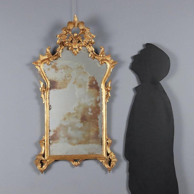 Mirror in Rococo style, crafted in Lombardy in the 20th century, featuring a carved and gilded wooden frame. The structure...