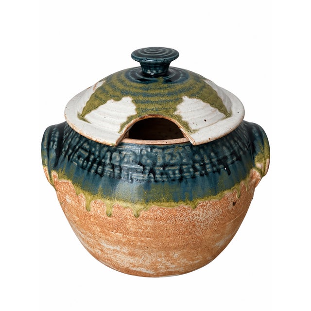 A signed handmade pottery soup tureen featuring a rounded body, sculpted side handles, and a coordinating domed lid with a...
