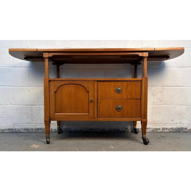 A stylish mid-century modern bar cart crafted in warm walnut with brass casters and matching brass handles. Features a...