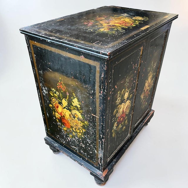 A charming Victorian black‑lacquered pine cabinet decorated with beautifully hand‑painted floral panels framed by gilt...