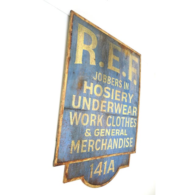 Reclaimed movie set sign made of wood in a tan and blue color. The sign reads "R.E.F., Jobbers in Hosiery Underwear Work...