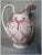 An Antique (circa 1910-1919) Art Nouveau Water Pitcher. The Water Pitcher is made of pottery and features a red transfer...