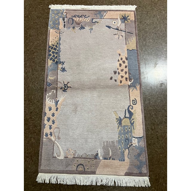 Hand-knotted Nepal wool rug featuring an open ivory field framed by a decorative border with stylized animal and abstract...