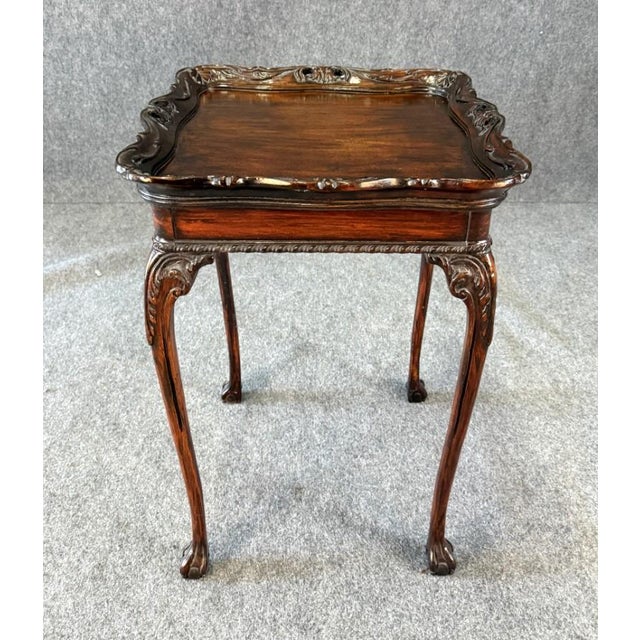 This early 1900s mahogany accent table features a richly finished top with an ornate, hand-carved scalloped edge and...
