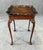 This early 1900s mahogany accent table features a richly finished top with an ornate, hand-carved scalloped edge and...
