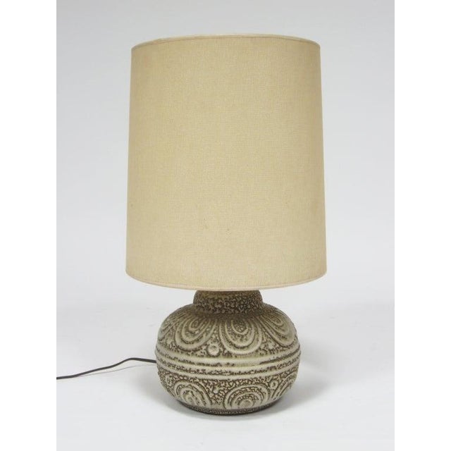 A delightful design, this table lamp features a ceramic base that has a richly textured and patterned surface. It is...