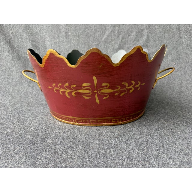 Vintage hand painted maroon and gold oval tole cachepot with a monteith top and two side handles. It measures...