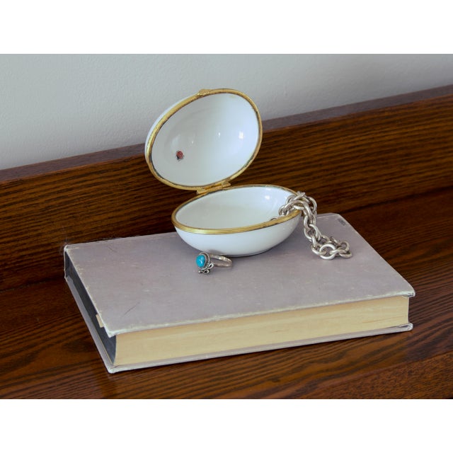 An oval hinged keepsake box in white glazed French porcelain, mounted in gilt brass with a scalloped shell thumbpiece. The...