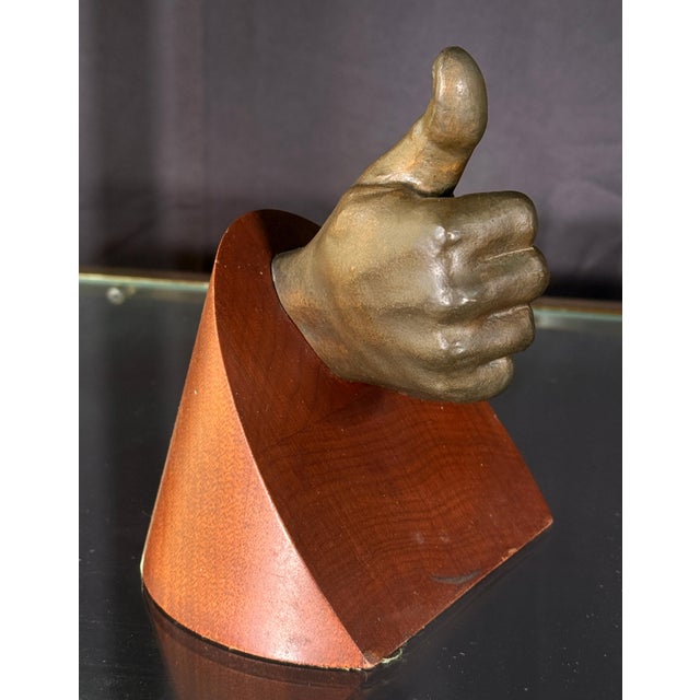 This small cast bronze sculpture depicts a naturalistic hand giving a thumbs up, mounted through a angled triangular...