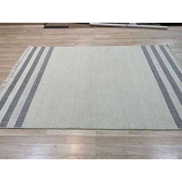 This handcrafted wool rug features a versatile palette of ivory, beige, cream, and white tones. Constructed as a flat...