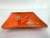A mid-century ceramic ashtray featuring a vibrant red-orange glaze accented with gilt floral motifs and subtle speckling...
