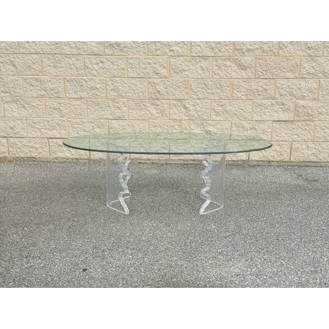 unique coffee table features a sculptural lucite base with a wavy design, supporting a sleek oval glass top