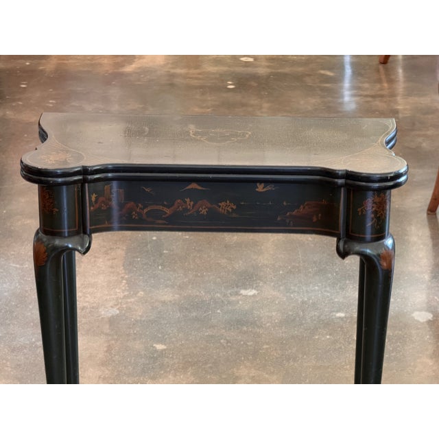 An English game table in dark green lacquer with gilt chinoiserie decoration — pagodas, bridges, and figures across the...