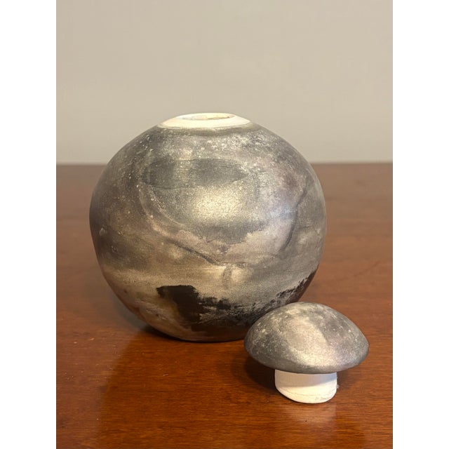 This vintage mid-century modern studio pottery vessel features a compact, rounded form with a fitted lid, emphasizing...