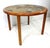 A darker teak wood framed round dining table with pole styled legs and having a colorful earth tones and blue detailed...
