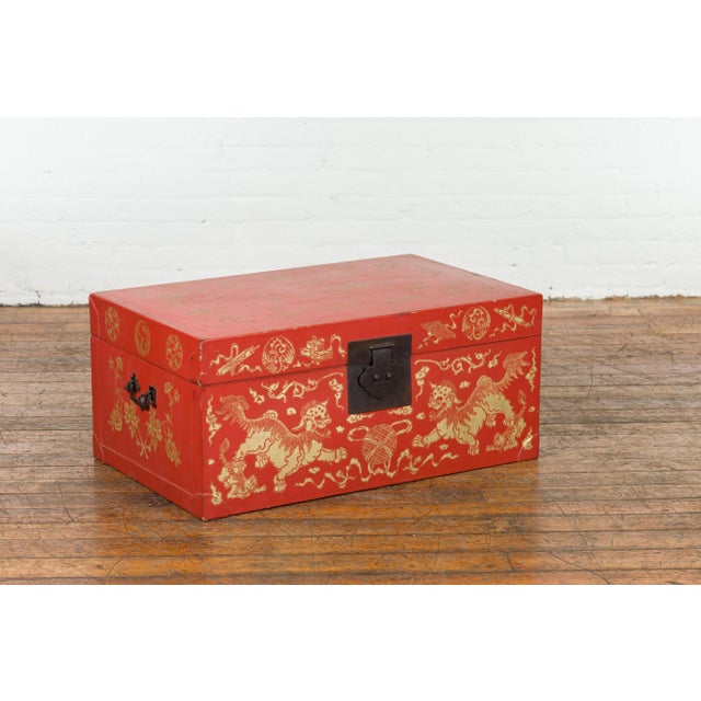 A Chinese red lacquered blanket chest from the 20th century, with gilt décor depicting guardian lions, flowers, scrolling...
