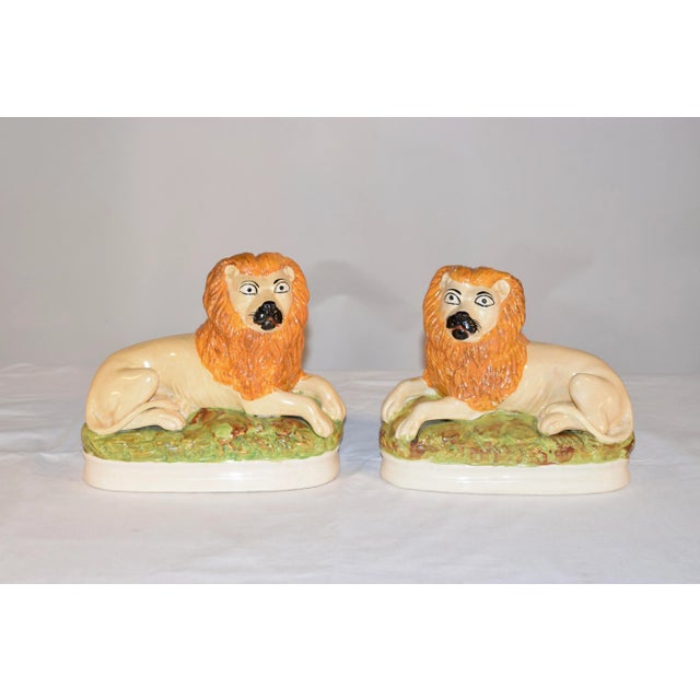 Pair of rare Staffordshire lion figures from England. The figures are lying lions on beds of grass, with their tails...
