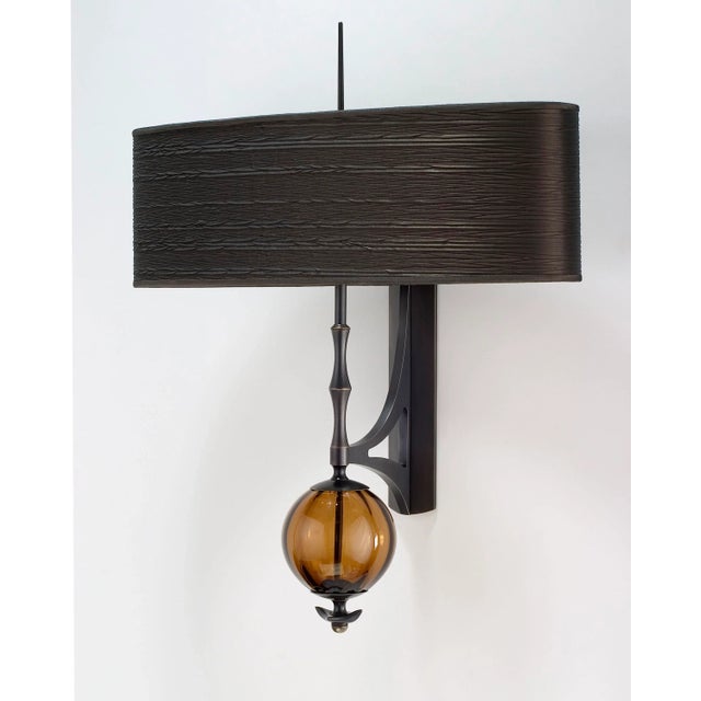 Each Metamorphosis Wall Sconce 5 is crafted individually from hand-blown amber glass, silk, and solid brass that has been...