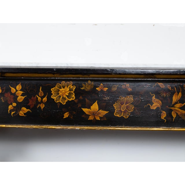 A pair of English Chinoiserie black and gold console tables from the 19th century with white marble tops. Embrace the...