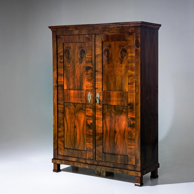 Large, two-door Biedermeier wardrobe veneered in walnut, featuring double-paneled doors and resting on plinth-mounted...