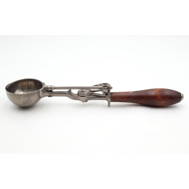 Vintage mechanical ice cream scoop historically called the ice cream disher or dipper. It features a wooden handle and a...