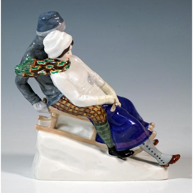Elegant sledging couple: the lady in a long purple skirt, white jumper and white bonnet, a long green patterned scarf...