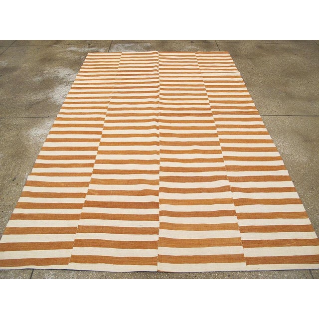 This Mid-20th century Turkish Flatweave Kilim rug, features a bold yet minimalist striped design in a warm palette of...