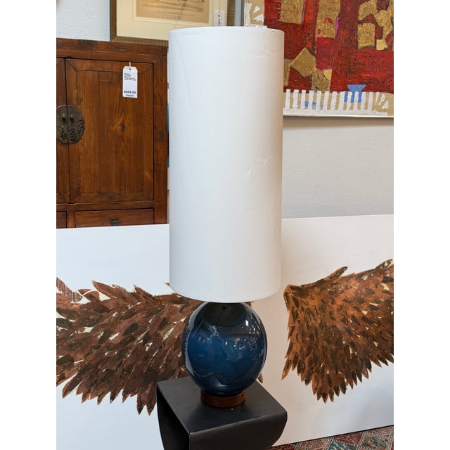 Design Plus Gallery presents a Ceramic Table from West Elm with Elongated Lamp Shade. The lamp is circular with a navy-...