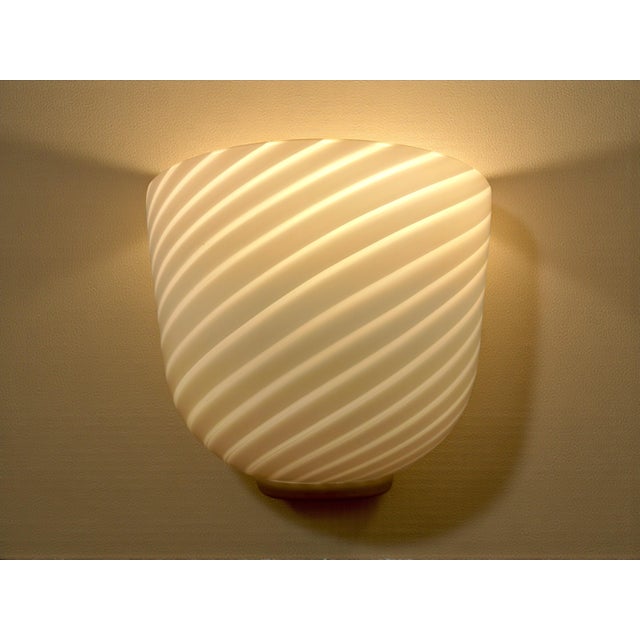 This wall lamp stands out for its modern and clean design: the white glass (milky/satin) is crafted with a "Swirl"...