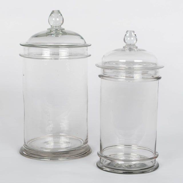A set of two French hand-blown clear glass lidded apothecary or candy jars. Smooth canister form, domed lid with knob....