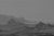 This artwork presents a stark, monochromatic landscape characterized by jagged mountains that loom in the distance,...