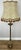 An elegant Vintage French standing lamp featuring a beautifully ornate gold-tone base and a large decorative fabric shade...