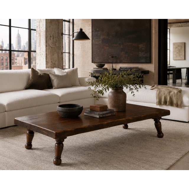 A substantial handcrafted rustic coffee table featuring thick solid wood slab construction, softly irregular hand-worked...