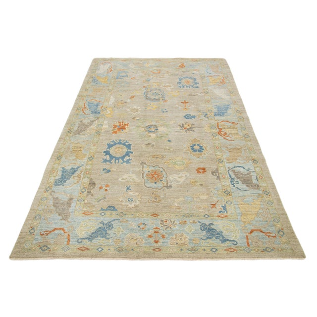 This hand-knotted wool rug has a light brown background and blue frame adorned with multicolor all-over designs. This rug...