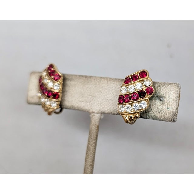Early 1980s goldtone lines of round faux-rubies and clear rhinestones clip earrings. Marked "TRIFARI" on cartouches on the...