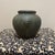 The vase showcases a distressed dark green and charcoal bronze patina finish, mimicking the weathered appearance of...
