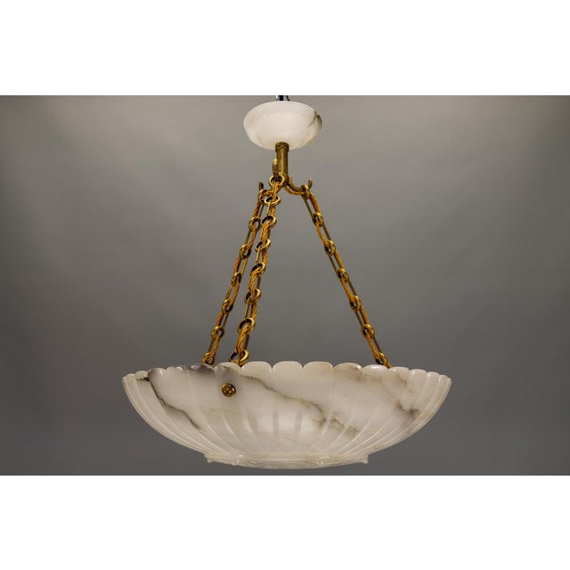 An impressive French Art Deco alabaster pendant light from the 1920s – sculptural in form, richly veined, and glowing with...