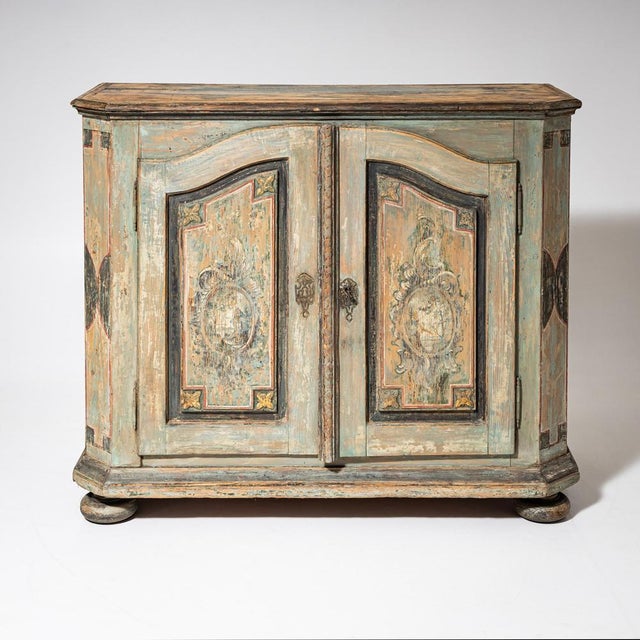 A two-door half cabinet in softwood featuring its original painted finish in pastel green and ochre tones. The front is...