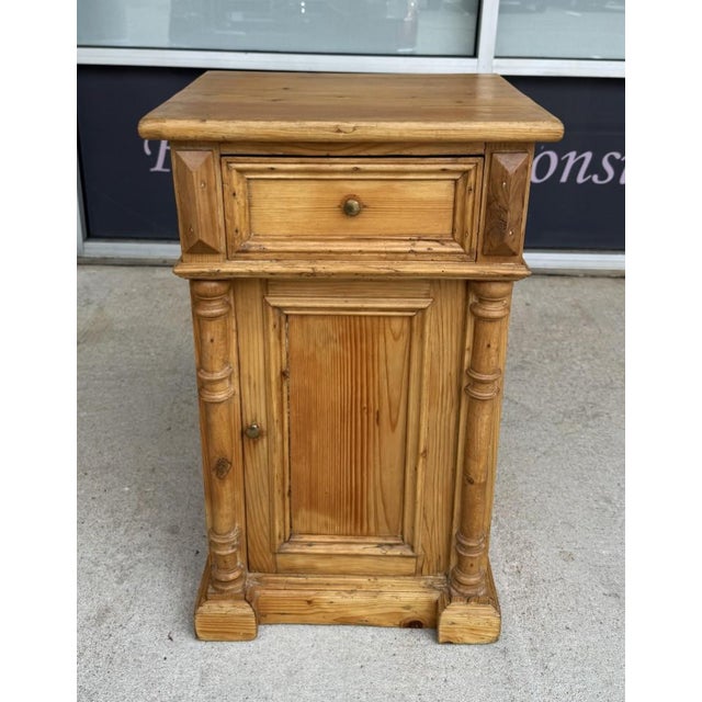 This early 1900s solid pine nightstand features a warm natural finish, paneled construction, turned side columns, and...